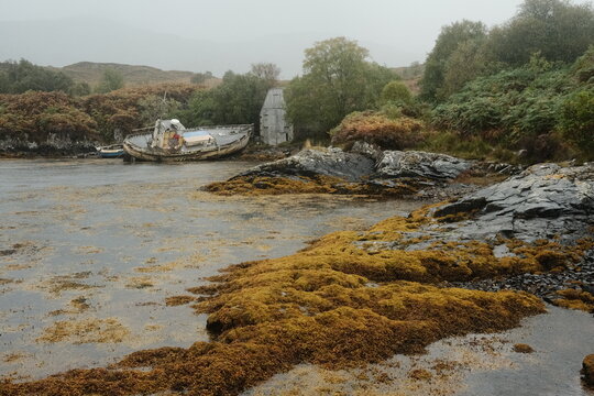 View of an abandoned boat resting on a rocky, seaweed-covered shore in Kyleakin, Scotland, United Kingdom.