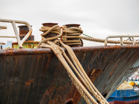 View of a weathered, rusty ship bow with thick mooring ropes secured to heavy metal bollards at the harbor in Busan, Busan, South Korea.