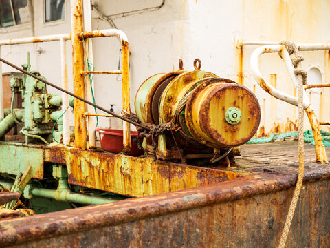 View of a weathered and rusty winch on the deck of a fishing vessel with ropes and metal railings in Busan, Busan, South Korea.