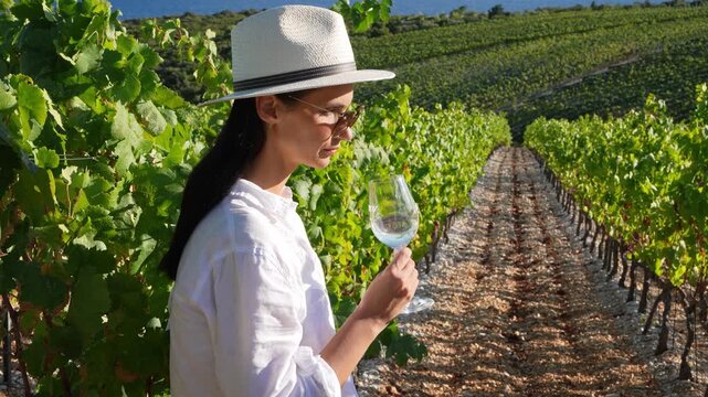 Woman tasting wine from a glass while standing in a sunny vineyard
