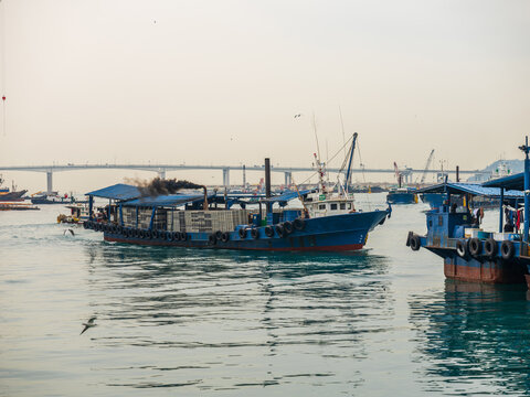 View of a blue cargo boat transporting goods through the harbor with a bridge in the background in Busan, Busan, South Korea.