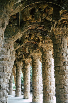 View of the stone colonnade and arched walkway in Park Guell, featuring rustic masonry columns and textured stone ceilings in Barcelona, Catalonia, Spain.