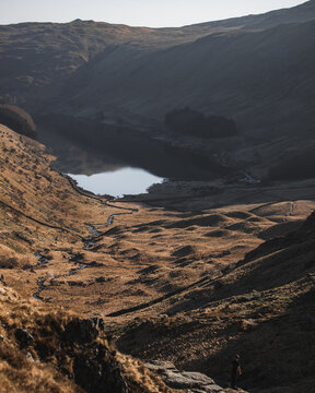 View of Haweswater Reservoir surrounded by rolling hills, stone walls, and a person standing on a rocky outcrop in Penrith, England, United Kingdom.