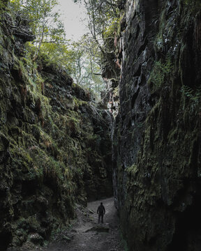 View of a person standing in the narrow, moss-covered chasm of Lud's Church with towering rock walls and lush ferns in Macclesfield, England, United Kingdom.