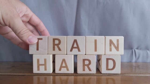 motivational word Train hard, laying out by hand from letters on wooden cubes, slow motion
