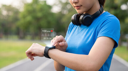 Obraz premium Female runner in blue checks heart rate on a smartwatch with a digital 158 BPM display at an outdoor track