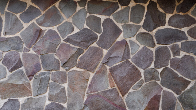 Natural dark stone slate wall texture with irregular flagstone pattern and cement joint lines for exterior architectural background