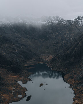 View of Loch Coruisk surrounded by dark, rugged mountains with snow-capped peaks and low-hanging clouds in the Isle of Skye, Scotland, United Kingdom.