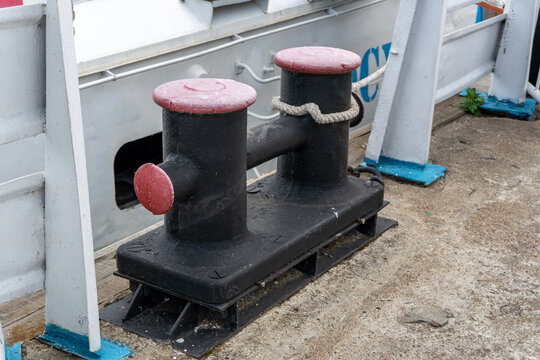 Black double mooring bitt with red caps on concrete dock