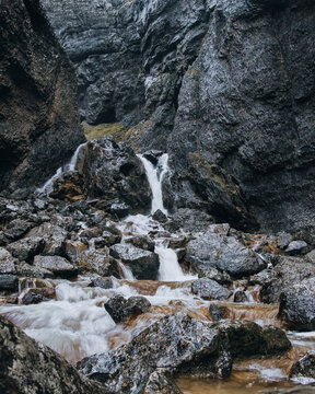 View of Gordale Scar featuring a cascading waterfall flowing over dark, rugged limestone rocks within a narrow gorge in Malham, England, United Kingdom.