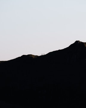 View of two hikers walking along a mountain ridge in Lake District National Park, England, United Kingdom.