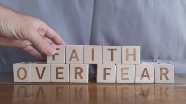 motivational word Faith over fear, laying out by hand from letters on wooden cubes, slow motion

