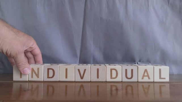 motivational word Individual, laying out by hand from letters on wooden cubes, slow motion
