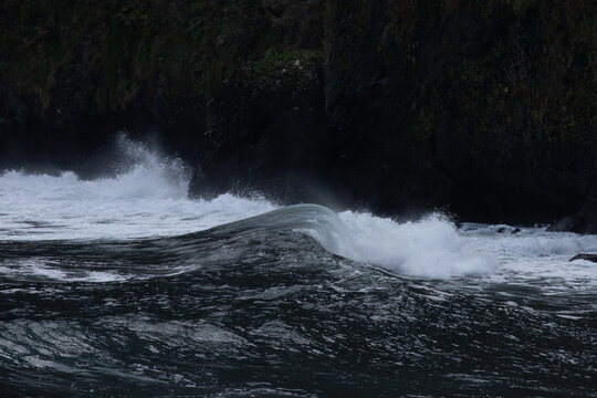 View of ocean waves crashing against dark rocky cliffs in Madeira, Portugal.
