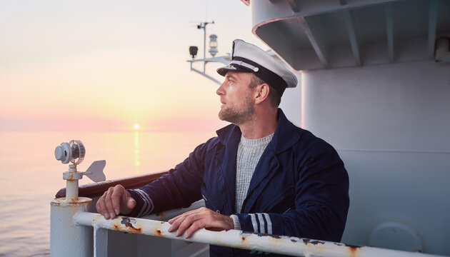 A sailor on a ship deck gazing at the sunset horizon.