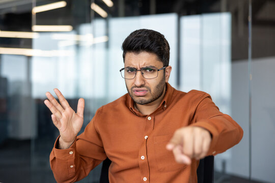 Frustrated businessman pointing at camera in office, angry professional man expressing disagreement or annoyance during a corporate meeting with negative body language and intense facial expression.
