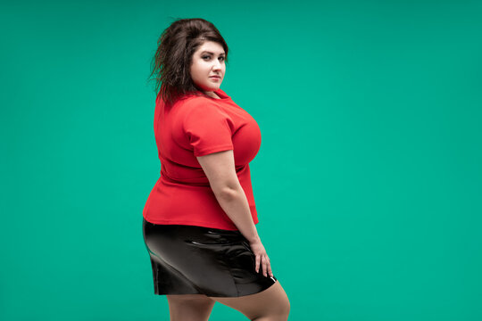 Plus size fashion model in red blouse and black skirt, fat woman on green background, body positive concept