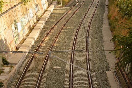Parallel railway tracks beside a graffiti-covered retaining wall