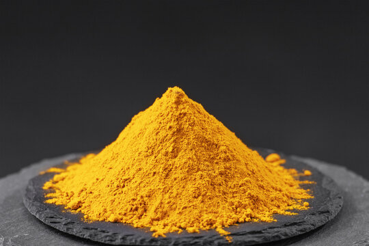 dried turmeric root powder or curcuma longa on a black slate stone tray