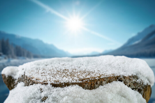 Empty covered with snow tree trunk for product placement, surrounded by fresh snow and a beautiful winter landscape in the background.
