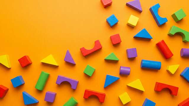 Scattered colorful wooden geometric building blocks in rainbow colors on bright orange background flat lay overhead view for creative kids play education construction toy and preschool learning