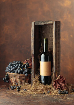 Bottle of red wine in old wooden box and blue grapes in basket.