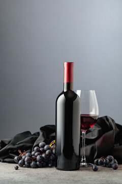 Bottle of red wine with grapes on a grey background.