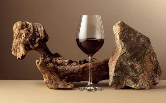 Glass of red wine with old driftwood and a piece of granite rock on a beige background.