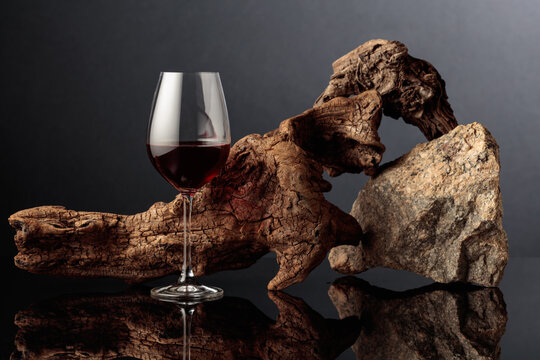 Glass of red wine with old driftwood and a piece of granite rock on a black reflective background.
