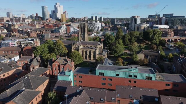 Aerial video overlooking red-brick residential quarters towards historic Leeds Minster and the expanding modern city skyline in morning sunlight.