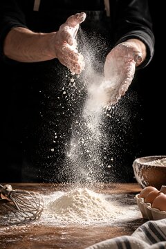 Chef sprinkling flour over dough on wooden table in professional kitchen setting with ample copy space