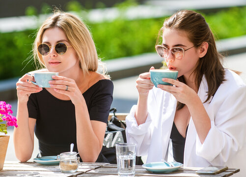 Outdoor cafe meeting with two women. Outdoor cafe coffee break with girlfriends. Female friends drinking cappuccino at outdoor cafe. Sharing news together at outdoor cafe.