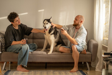 Man and teenage boy smile stroking their husky on sunlit sofa, generation gap closing over shared evening, conversation worth more than advice. Wide shot. Concept of generation talk of father and son © iwavephoto