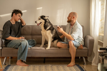 Father and son both reach to husky standing between them on sofa, generation talking instead of arguing, contact teenagers rarely allow. Wide shot. Concept of generation talk of father and son © iwavephoto