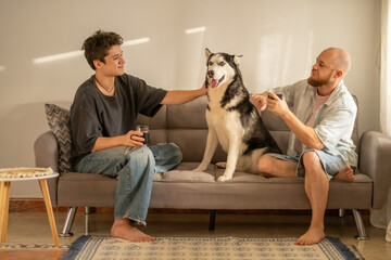 Laughing father and son spend weekend evening with dog at home, generation difference meaning nothing here, moment building real trust. Wide shot. Concept of generation talk of father and son © iwavephoto