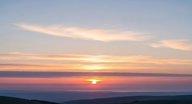 Breathtaking panoramic view of the sun setting over rolling hills casting a warm orange glow across the dramatic evening sky filled with soft clouds creating a peaceful atmosphere
