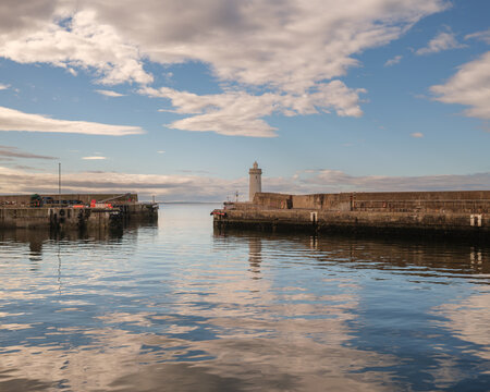 Bright sunlight shining over the harbour entrance and stone lighthouse of Buckie located in Moray on the coast of Scotland during a clear day