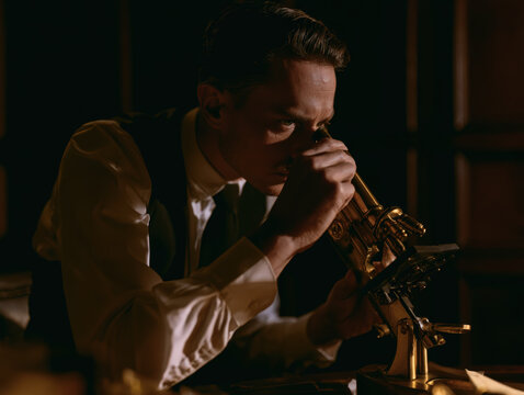 Microbiologist peering through vintage brass microscope in dark wood-paneled study, editorial styling, 35mm lens, natural depth of field