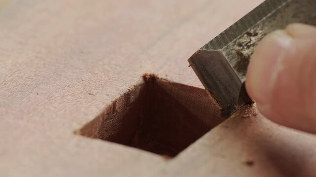 Gloved hand chiseling a precise square mortise joint into wood, close up joinery