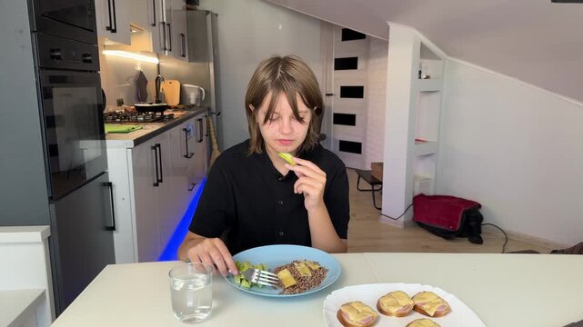 Young woman at kitchen table extends plate of savory pastries toward viewer. Counter, appliances, and neutral walls sit in background as soft warm indoor lighting supports calm inviting mood.