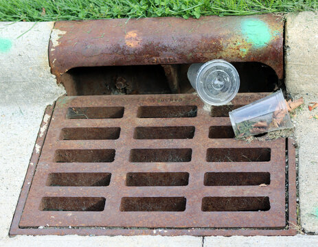 Cast iron storm drain inlet on concrete curb clogged with plastic trash and debris