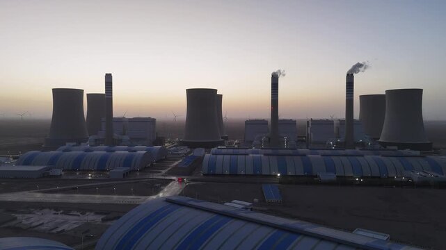 Large scale thermal power plant at dusk with cooling towers and smoke stacks