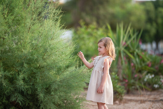 Young girl in pale dress touching feathery garden foliage outdoors in summer