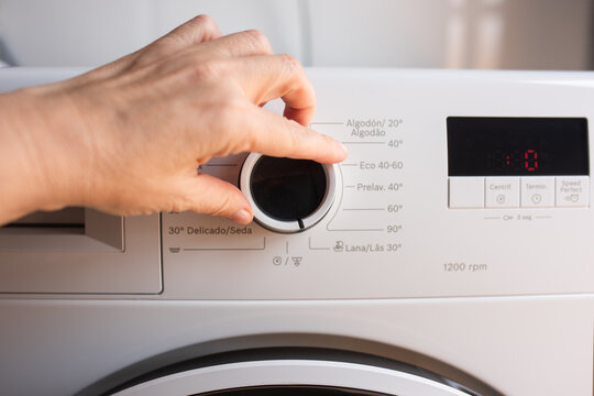Hand Adjusting Washing Machine Dial with Digital Display in Home Laundry Appliance Closeup