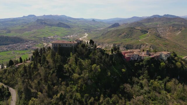 Stunning aerial drone panorama of medieval Montebello Castle perched on a rocky hill surrounded by lush green valley and historic village in Poggio Torriana, Emilia-Romagna, Italy