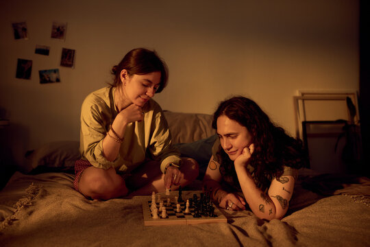 Young Caucasian couple playing chess board game on bed at home. Concept depicts domestic leisure, romance, indoor entertainment, useful for couple relationship and lifestyle marketing