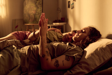 Young adult Caucasian romantic couple lying in bed resting together and holding hands at home....