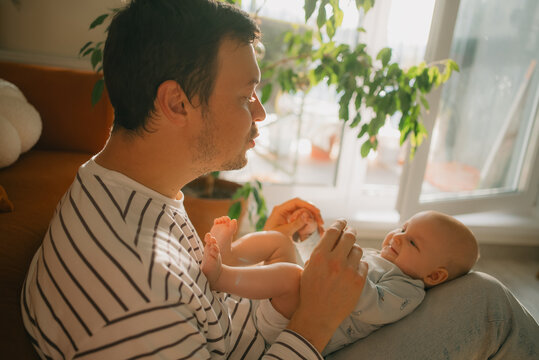Father holding his happy newborn baby on his lap, looking at the child with affection, strengthening their bond during a tender family moment in the light filled home