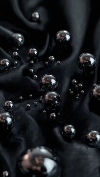 Dark chrome spheres vibrating on black surface under cold macro lighting