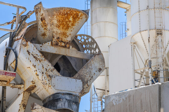 Close-up of a rusty concrete mixer truck chute against industrial silos